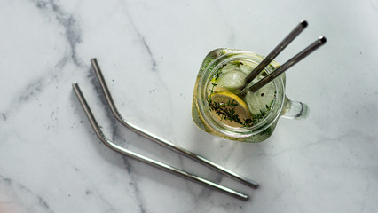 Metal drinking straws and cold drink in glass mason jar on white marble background. Top view or...