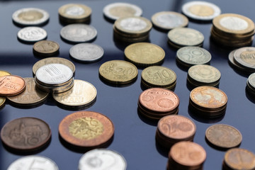 Coins from different countries are laid out on stacks on a blue background. Close-up at an angle.