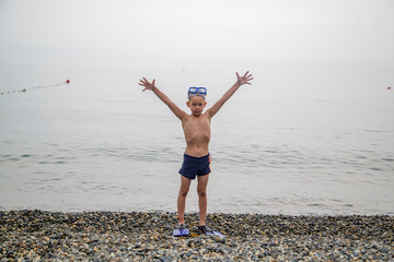 happy boy in mask and flippers for diving stands on the seashore
