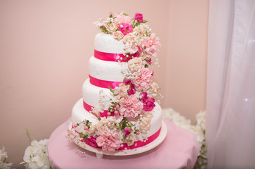 beautiful white wedding cake with fresh pink flowers and crimson ribbon
