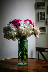 Gorgeous white and pink pions in a glass vase on the table with some light in front of the Parisian window