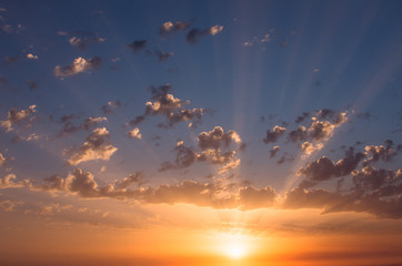 Fototapeta premium Orange sunset sun and rays through the clouds against the blue sky.