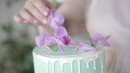 Confectioner neatly decorates turquoise wedding biscuit cake with pink orchid