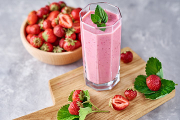 Smoothie with summer strawberry in glass jar and fresh berries on a gray background
