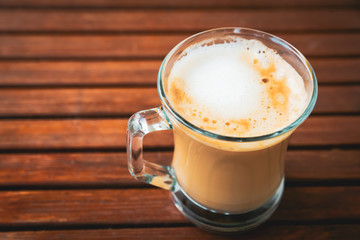 Cup or glass of coffee with white foam on wooden brown table, with copy space, top view