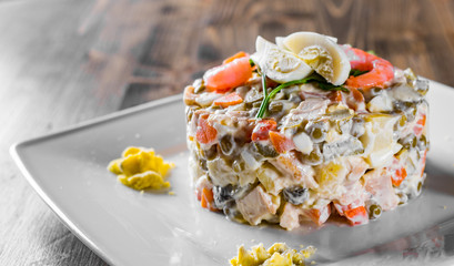 Olivier salad with shrimps, eggs and vegetables in a plate on wooden table