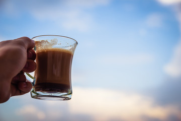 Man hand raising glass with morning coffee. Starting a good day concept. With cloudy sky in the background