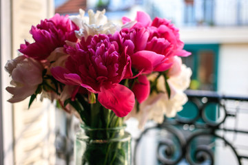 Gorgeous white and pink pions in a glass vase in sunset light in front of the open Parisian window