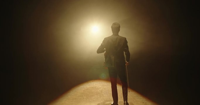Professional violin player making steps on stage before performing a solo during concert. spotted by light on black background 4k footage