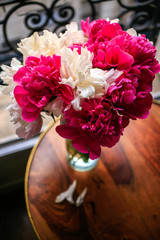 Gorgeous white and pink pions in a glass vase in sunset light in front of the open Parisian window top view