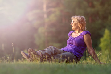 Side view woman sitting in grass and enjoying the sunshine in nature camping