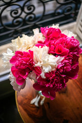 Gorgeous white and pink pions in a glass vase in sunset light in front of the open Parisian window top view