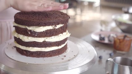 confectioner puts on a chocolate sponge layer of cake on a cream inner layer