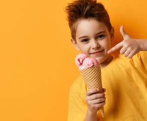 Baby boy kid eating strawberry ice-cream in waffles cone happy screaming laughing on yellow background