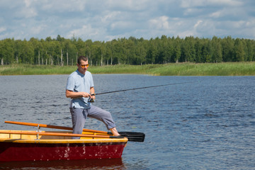 a man in yellow glasses, in a boat with oars, in the center of the lake, holds a fishing pole to...