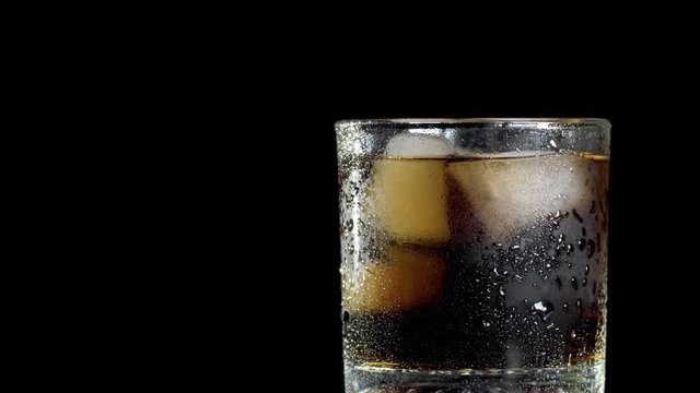Cola with ice cubes in glass over black background. Cola with bubbles being poured in glass. Rotate glass of Cola fizzy drink isolated on black background.