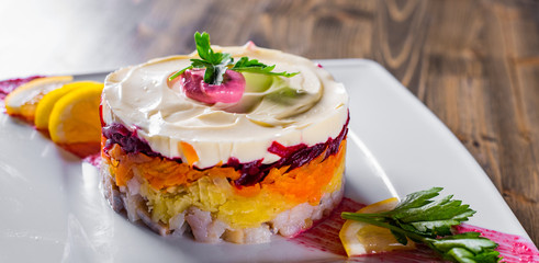 layered salad with herring, beets, carrots, onions, potatoes and eggs close-up on a plate on wooden table