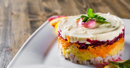 layered salad with herring, beets, carrots, onions, potatoes and eggs close-up on a plate on wooden table