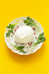 Burrata, Italian cheese with tomatoes, spices, argugula and olive oil and balsamic vinegar / yellow background