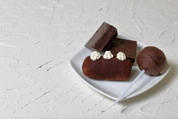 Chocolate cake pops and pieces of black chocolate on a white plate. Next to the potato cake. On the surface covered with white decorative plaster.