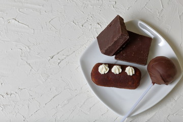 Chocolate cake pops and pieces of black chocolate on a white plate. Next to the potato cake. On the surface covered with white decorative plaster.