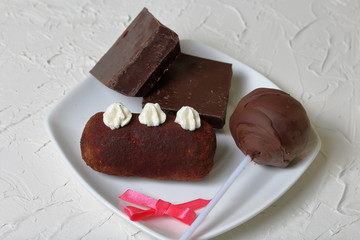 Chocolate cake pops and pieces of black chocolate on a white plate. Next to the potato cake. On the surface covered with white decorative plaster.