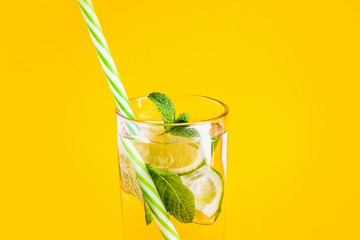 Fresh summer lemonade with water, lime and mint in a glass tumbler with a straw on a yellow background. Cold, refreshing summer cocktail close up. Fresh drink with copy space
