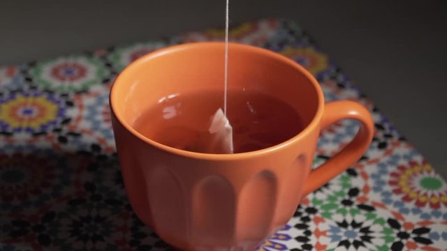 Italy - June 23, 2019: Tea bag dipped in hot water contained in an orange cup to prepare a hot drink.