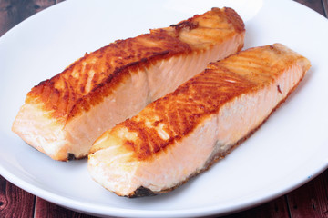2 Grilled salmon steaks on white plate served on wood.