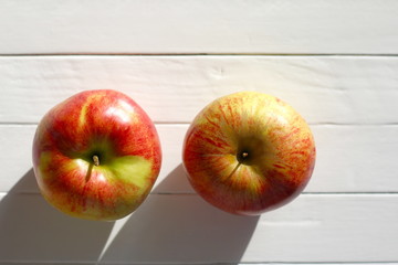 Two apples on an old white wooden table in the sunlight