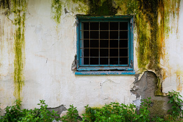 Broken blue window with metal frame on a damaged white wall