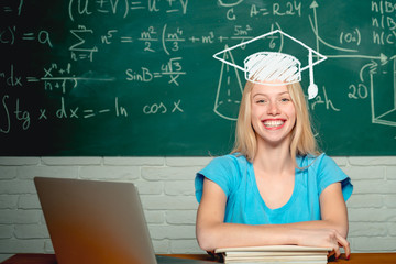 Happy student. Woman working on laptop computer over chalkboard background. College Student. Student sitting at table and writing on notebook