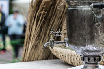 Old samovar with traces of repair crane on the background of a basket and a bundle of straw.