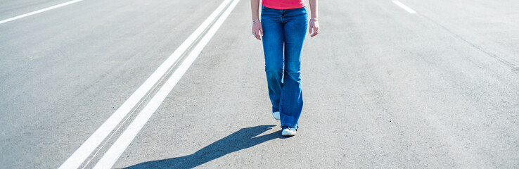Woman legs in jeans and sneaker shoes walking on the empty road