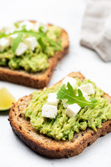 Healthy bread toast with mashed avocado and feta cheese topped with arugula leaf. Closeup view, selective focus