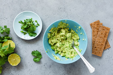 Mashed avocado in bowl and rye crispbreads. Making guacamole sauce, healthy vegetarian appetizer or snack. Top view