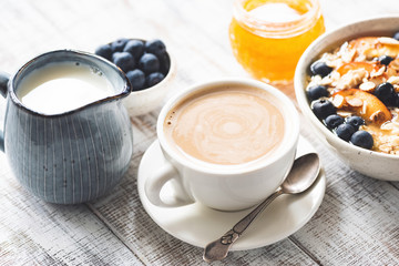 Breakfast table. Oatmeal porridge with fruits and berries, jar of honey, coffee with cream. Healthy food, clean eating concept
