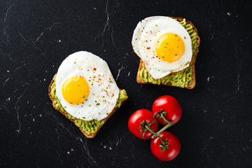 Sunny side up egg and avocado on whole grain toasted bread on black marble table background. Top view