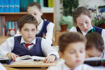 A young schoolboy sitting at a desk in a school class.