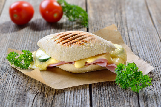Getoastetes und im Kontaktgrill gepresstes italienisches Panini mit Schinken, Käse und Gemüse - Pressed and toasted panini with ham, cheese and vegetables served on sandwich paper 