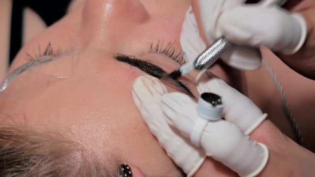 Close-up of cosmetologist making microblading procedure. Permanent makeup. Permanent tattooing of eyebrows. Cosmetologist applying permanent make up on eyebrows- eyebrow tattoo.