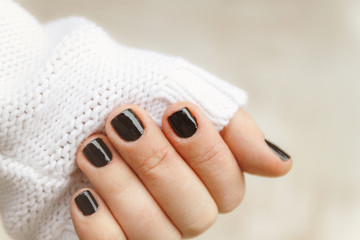 hand with black manicure on short nails in a white sweater on a light background. The concept of a...