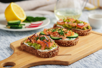 healthy open sandwiches with  rye bread  salmon cream cheese sliced cucumber dill avocado on wooden...
