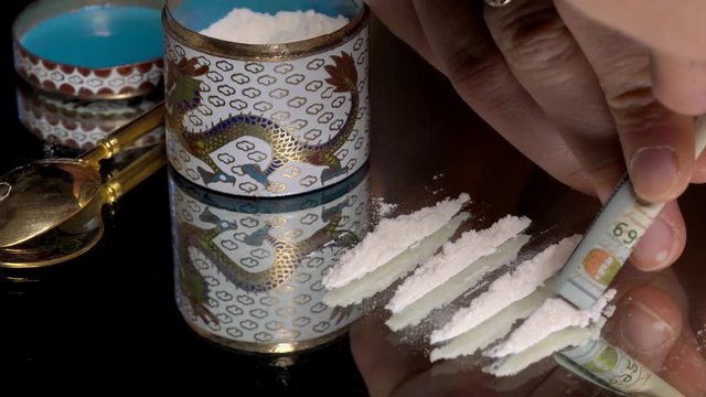 This closeup video shows a person snorting lines of cocaine drugs using a rolled hundred bill.