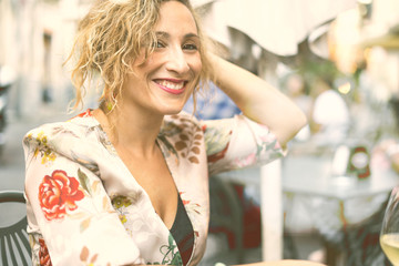 Portrait of an attractive adult woman drinking with friends sitting on an outdoors wine bar. Looking at camera. Adult people free time.