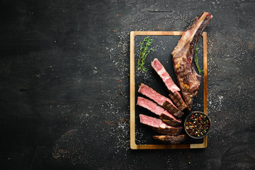Grilled steak on the bone sliced, herbs and spices on Wooden background. Barbecue. Top view. Free...