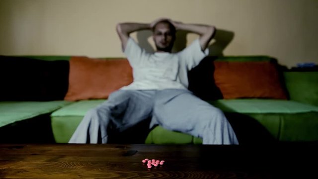 Depressed man suffering from suicidal depression want to commit suicide by taking strong medicament drugs and pills pain killers while he sitting in his dark room selective focus moody dramatic look