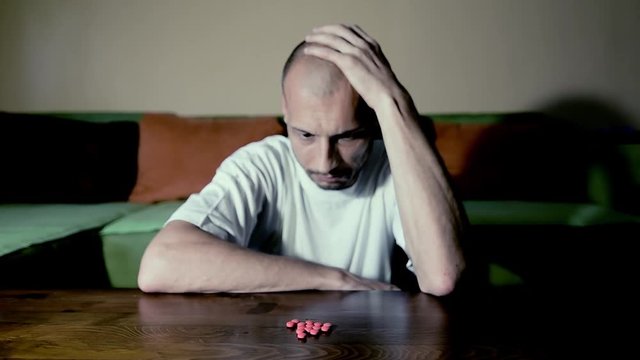 Depressed man suffering from suicidal depression want to commit suicide by taking strong medicament drugs and pills pain killers while he sitting in his dark room selective focus moody dramatic look