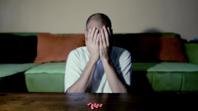 Depressed man suffering from suicidal depression want to commit suicide by taking strong medicament drugs and pills pain killers while he sitting in his dark room selective focus moody dramatic look