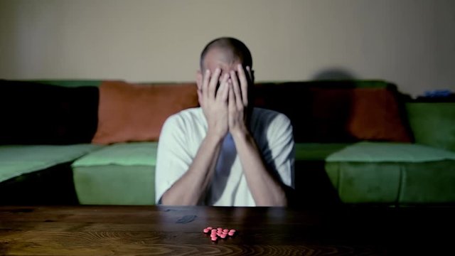 Depressed man suffering from suicidal depression want to commit suicide by taking strong medicament drugs and pills pain killers while he sitting in his dark room selective focus moody dramatic look